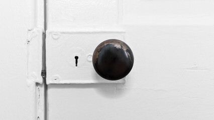 Close up profile photo of an old vintage round metal door knob with tarnished finish on a heavily painted wooden door with a skeleton keyhole lock and copy space.