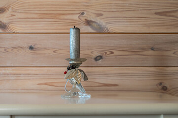 Silver color candle in the glass and metal candlestick holder on wooden wall background.