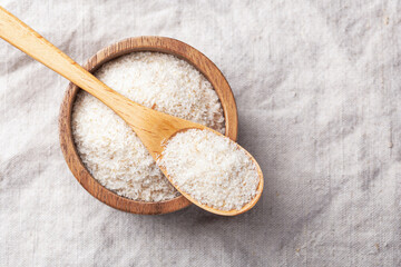 Psyllium husk in spoon and wooden bowl on linen table cloth background, top view