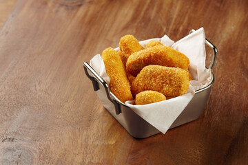 A portion of chicken nuggets served in a unique tin container with white napkin on a wooden table