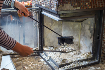 Cleaning the fireplace. Ash and charred piece of wood lying on the blade with a long handle closeup