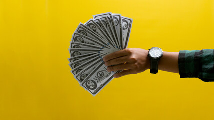Close-up of a hand holding banknotes against a bright yellow background. Ideal for illustrating...