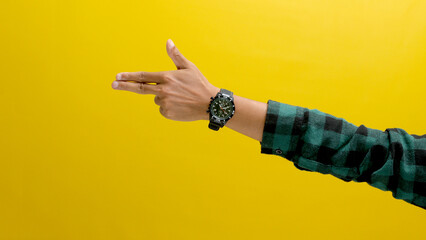 Hand wearing a wristwatch makes a finger gun gesture. Isolated on a yellow background.