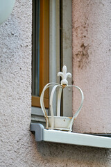 Kleine, weiße Krone oder Krönchen mit Rost steht als Deko, Dekoration auf einem Fensterbrett vor einem Fenster in der Hauswand
