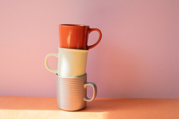 Stack of mug cups on orange shelf. pink wall background