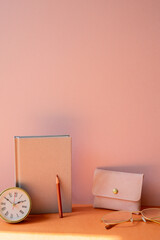 Workspace desk with notebook, clock, pencil, pouch, eyeglasses. pink orange background