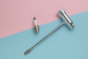 A special key and a short spark plug on a pink and blue background.