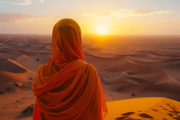 Person draped in orange cloth watching sunset over desert, capturing a moment of awe and contemplation.


