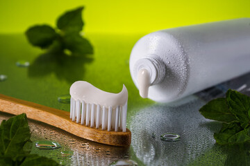 Close up tube of toothpaste and bamboo toothbrush on wet reflective surface with fresh mint leaves....