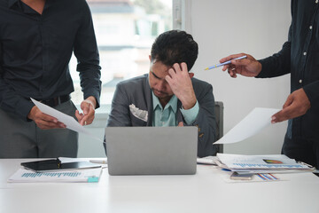 Tired Asian young businessman. Stressed. The man at work has a headache from overwork. Calculating with a calculator with piles of paperwork being handed over in the office. Overtime work.