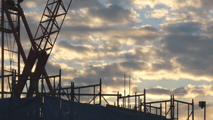 Morning at the construction site: clouds and a large crane shining in the dawn light