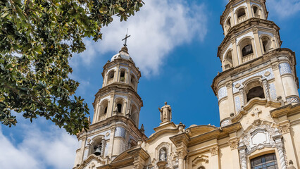 An old colonial building in the historic quarter of Buenos Aires. The Church of San Pedro Gonzalez Telmo. Towers with bells, crosses, sculptures, arches, ornaments against the blue sky and clouds.