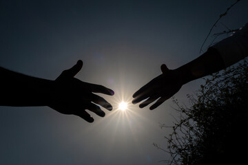 Silhueta de duas mão em que a mão feminina em meio a silvas e às adversidades da vida pede ajuda...