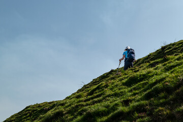 Mulher turista a caminhar de paus na mão numa montanha com uma forte inclinação num dia...