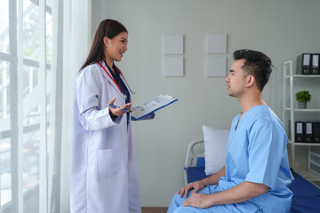 Physiotherapist giving advice and encouragement to male patient doing physiotherapy lying on...