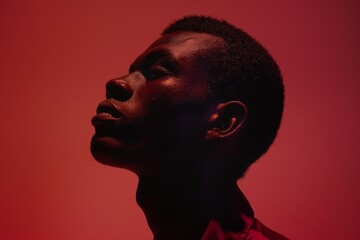 Portrait of a Black man in red light, looking upward thoughtfully. Ideal for themes of...