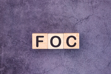 FOC word made with building blocks on a grey background. Abbreviation of Free of charge.