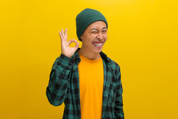 Excited young Asian man, dressed in a beanie hat and casual shirt, blinks at the camera while...
