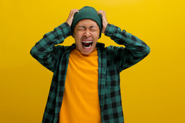 Frustrated young Asian man, wearing a beanie hat and casual outfit, is screaming while holding his...