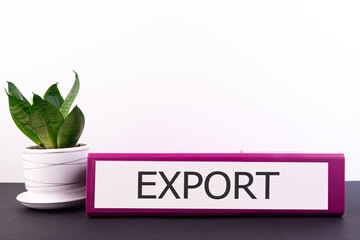 EXPORT word concept written on a folder lying on a dark table with a flower in a pot on a light...