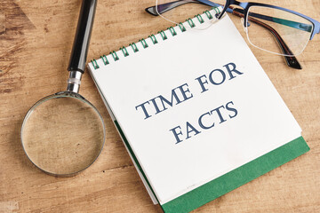 Time for facts message written on a notebook with a magnifying glass and glasses on a vintage...