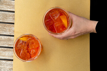 a woman's hand holds a glass of aperol spritz with ice and Prosecco, a traditional Italian...