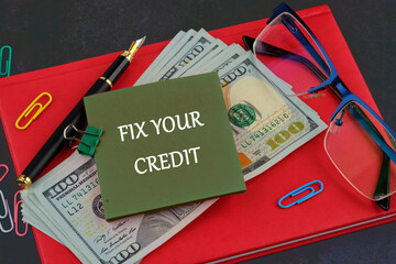 FIX YOUR CREDIT text written on a sticker on the background of a business notebook and dollars