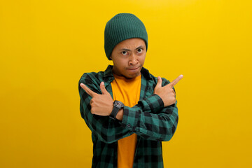 an Upset young Asian man is seen pursing his lower lip and crossing his arms while pointing in different direction, showing hesitation and difficulty in making a choice, isolated on yellow background