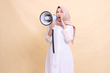 woman asian mature wearing a candid hijab screams angrily holding a loudspeaker megaphone while...