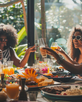 friends seated around a table, brunch spread in front of them, mimosa glasses raised in a toast