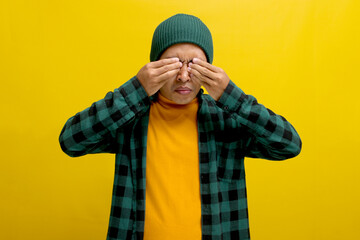 Young Asian man in a beanie hat and casual shirt is experiencing discomfort with his contact lenses, rubbing his swollen eyes due to a dust allergy, causing itching. Healthcare and medical concept.