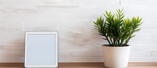 A digital tablet potted plant and books are placed beside a white brick wall creating an aesthetically pleasing copy space image