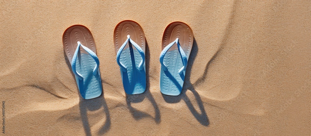 Poster A top view image of flip flops resting on the sandy beach with a blue background providing copy space