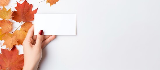 A female hand holds a blank card while surrounded by autumn leaves on a white background img copy space image