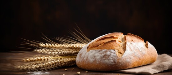 A close up image of homemade bread with a rustic peasant round shape and wheat spikelets surrounding it leaving room for text The bread appears sliced placed on a wooden chopping board and accompanie