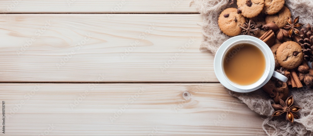 Poster Hello winter A cozy scene unfolds on a light wooden background featuring a cup of tea a scarf delectable cookies and tempting hazelnuts Perfect for a copy space image
