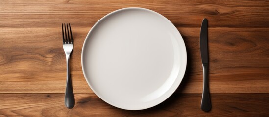 A concept image of white plate fork and knife placed on a wooden table along with cutlery and silverware. Creative banner. Copyspace image