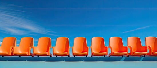 Close up copy space image of a row of vacant orange seats in a sports stadium set against a...