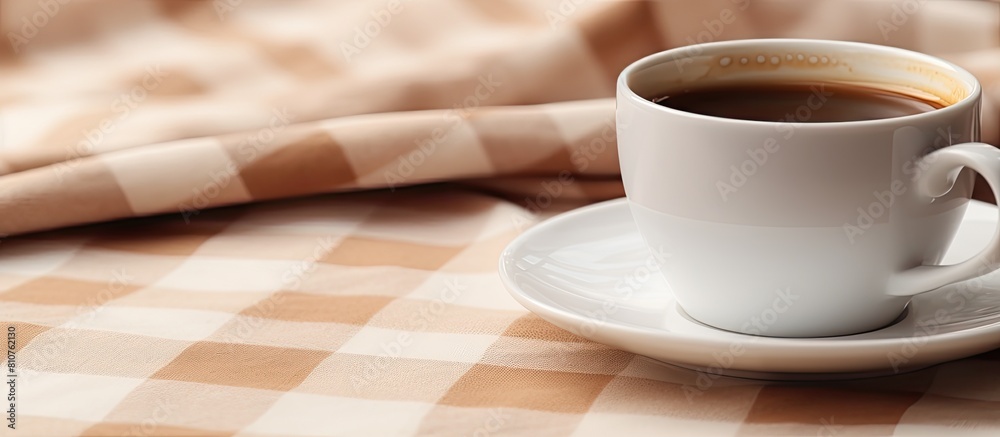 Poster Copy space image of a white coffee cup resting on a plaid tablecloth with subtle cream brown and beige tones creating a shallow depth of field effect