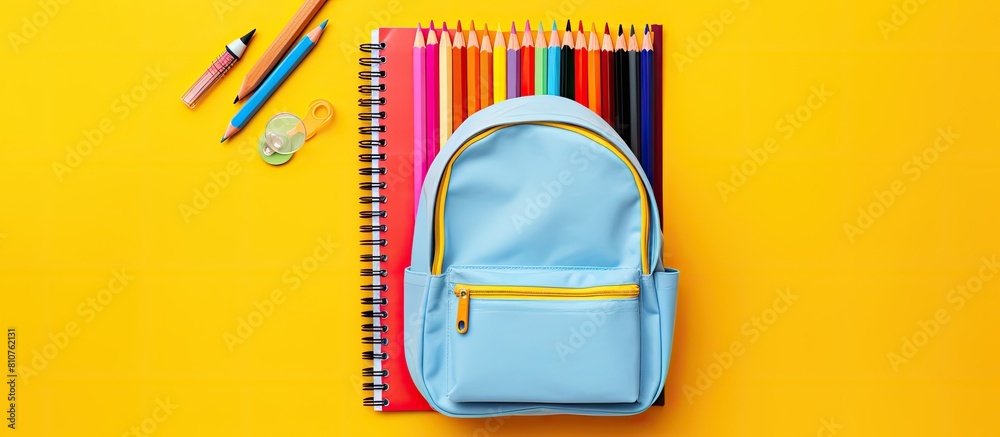 Poster top view image of a yellow backpack filled with school supplies including a notebook pens an eraser 