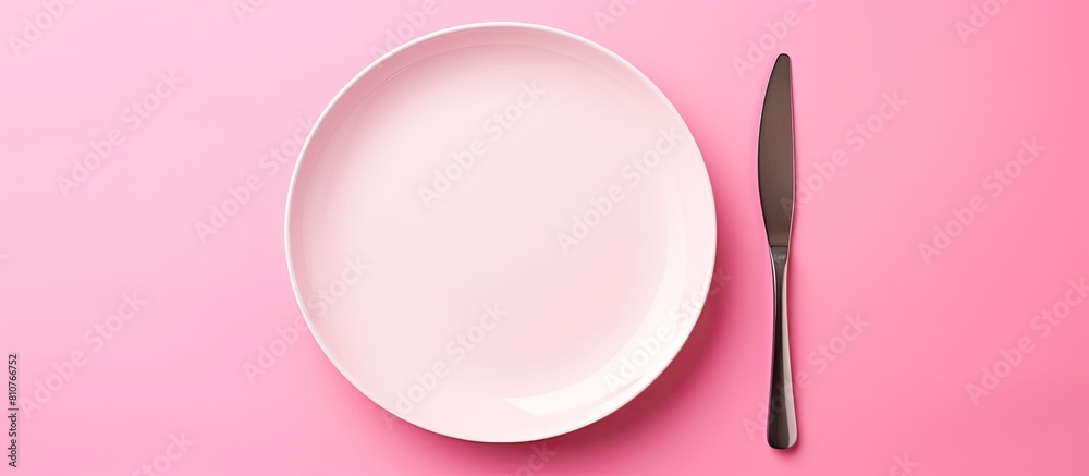 Poster A top down view of a white round ceramic plate on a pink background with a fork and knife elegantly positioned alongside it creating a captivating copy space image