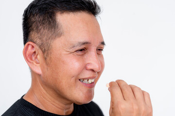 A confident Asian man in his forties smiles as he takes a chewable antacid tablet. Perfectly isolated on a white backdrop.