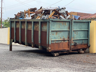 A dump truck bin  full of rubbish and materials placed nearby a building.