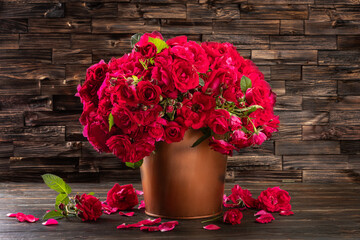 A large bouquet of red roses sits in a brown vase on a wooden table