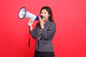 The expression of an indonesia female manager tilted to the right, screaming in surprise, using a megaphone, holding a mic to the camera, wearing a gray jacket and a red skirt.for advertising concepts