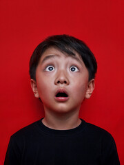 Surprised Asian boy with wide eyes on a red background. Surprised face of a child with open mouth - obrazy, fototapety, plakaty