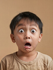 Surprised Asian boy with wide eyes on a beige background. Surprised face of a child with open mouth - obrazy, fototapety, plakaty