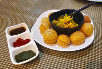 Pani Puri, served with tamarind, mint chutney, and a spiced filling on a white plate