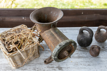 An old-fashioned manual grinder sits on a weathered wooden bench beside a basket filled with dried...
