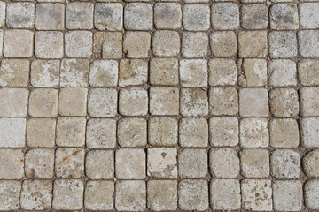 captures a close-up view of a cobblestone pavement, showcasing a pattern of square stones in various shades of gray and beige. The stones exhibit a weathered texture, indicating age